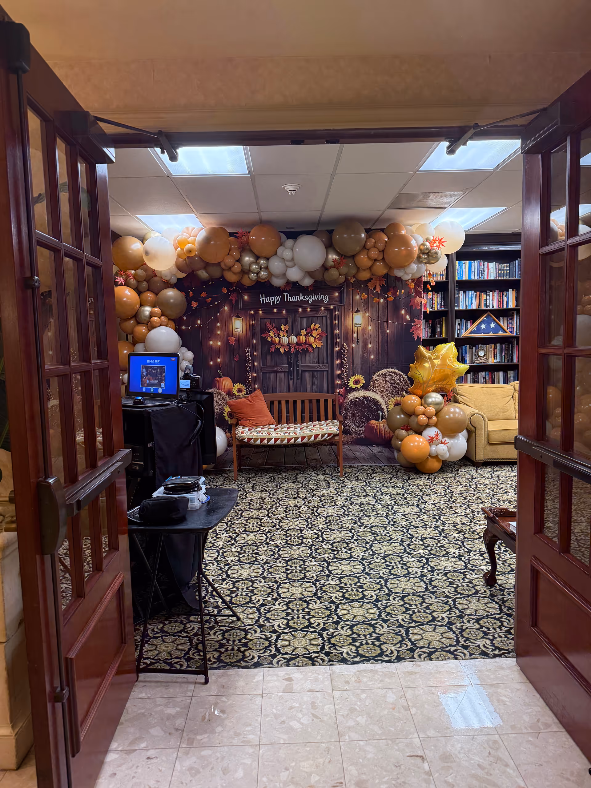 Indoor event space with a Thanksgiving backdrop, balloon arch, bench, sofa, and bookshelves.