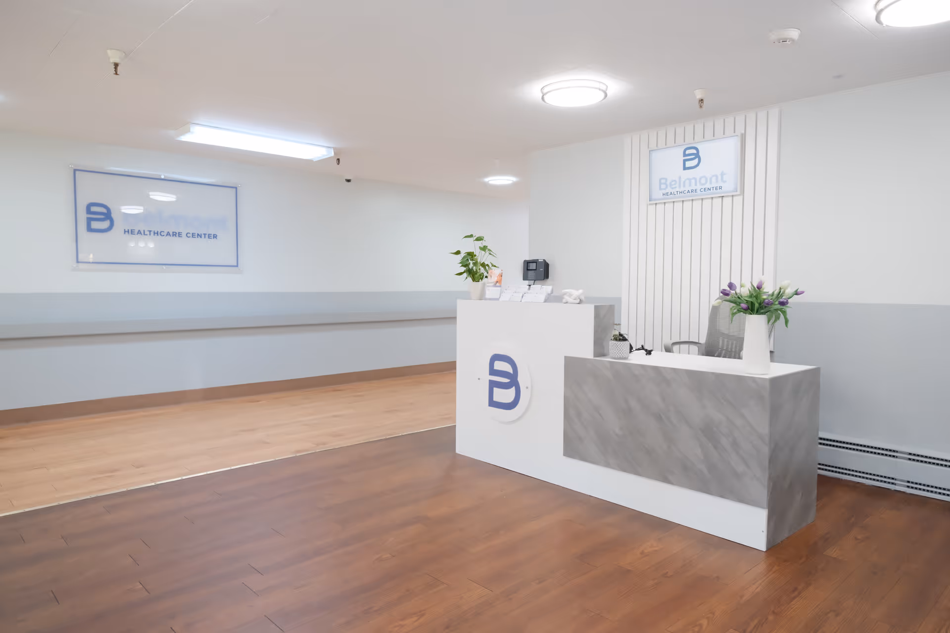 Bright lobby with a modern reception desk, signage, and potted plants.
