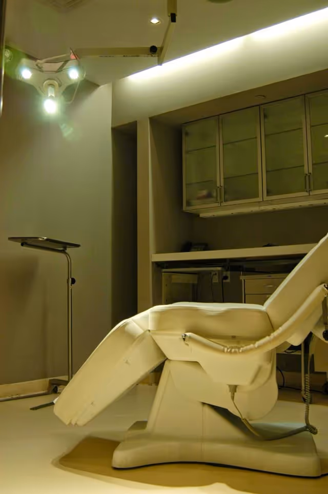 A white reclining medical chair in a sterile treatment room with cabinets.