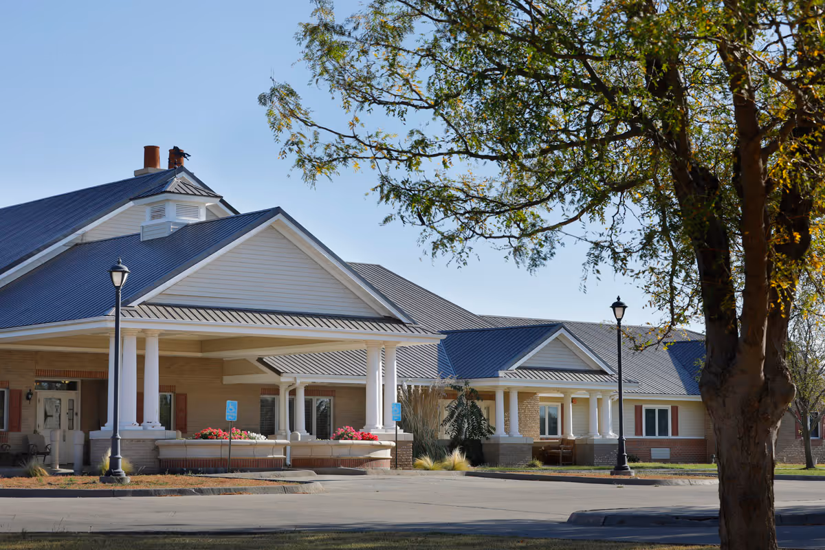 Front view of a single-story assisted living facility with pillars and a blue metal roof.