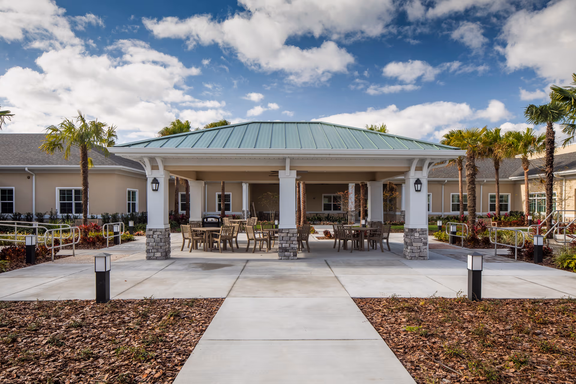 Exterior view of The Club at Lake Gibson seating area with tables, chairs, and palm trees.