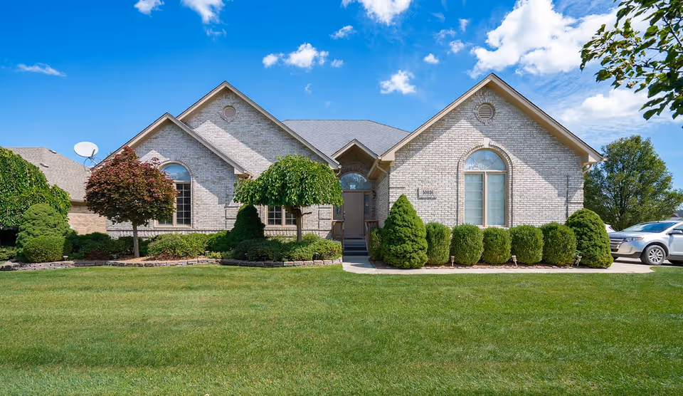 Brick senior living facility front with manicured lawn, shrubs, and a driveway.