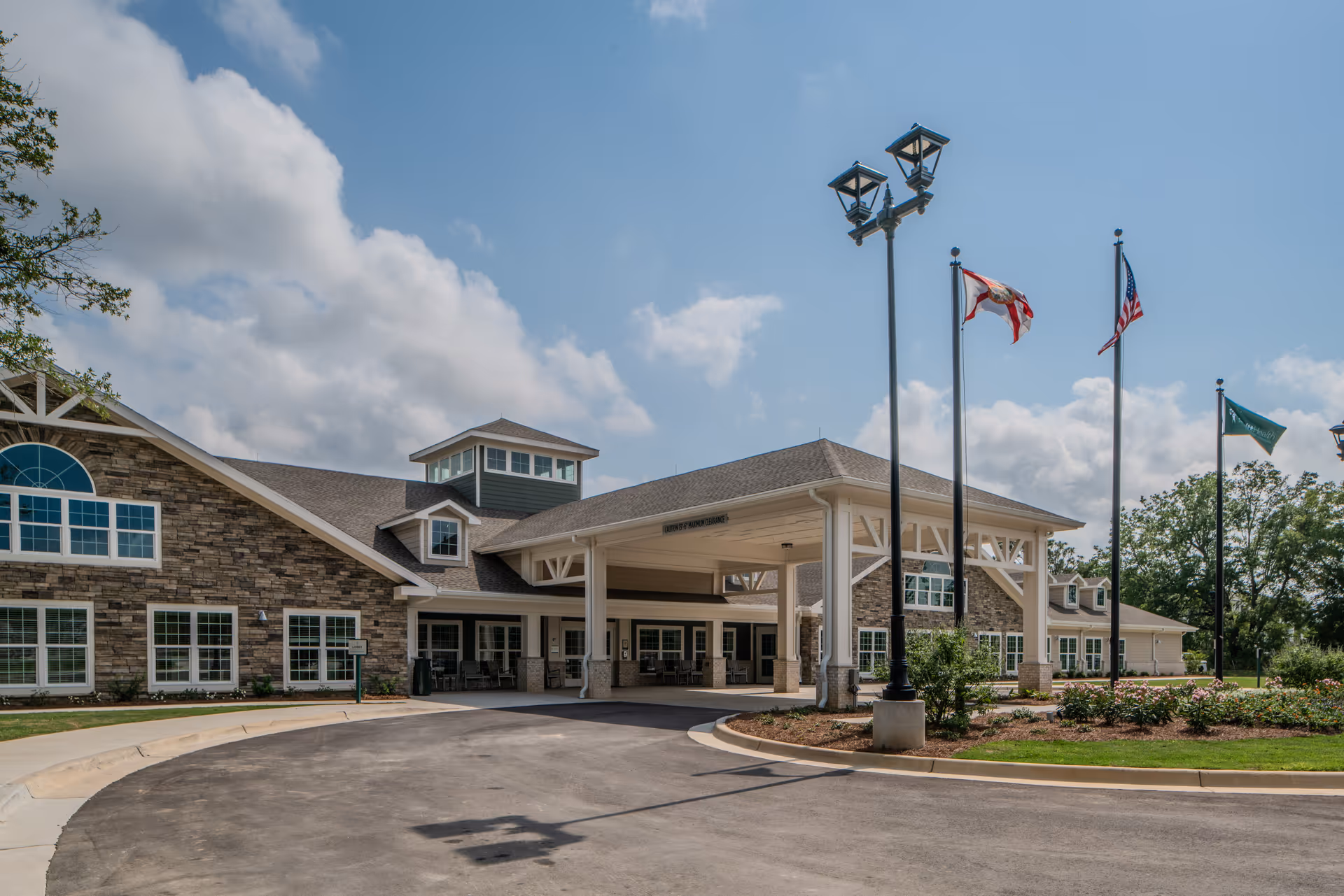 Exterior view of a PruittHealth Pensacola building entrance with flagpoles and drive-up canopy.
