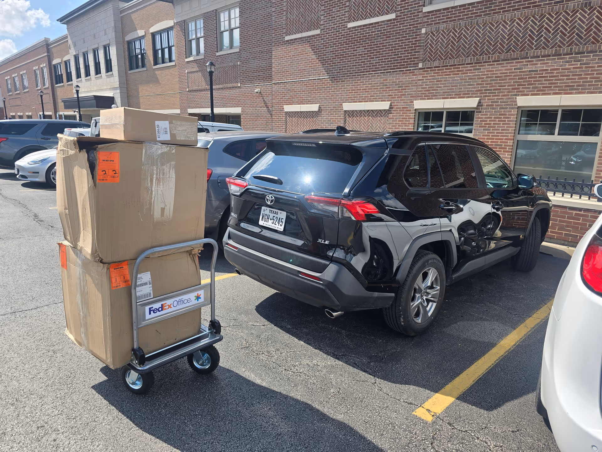 A delivery dolly with packed boxes beside a black SUV in a parking lot.