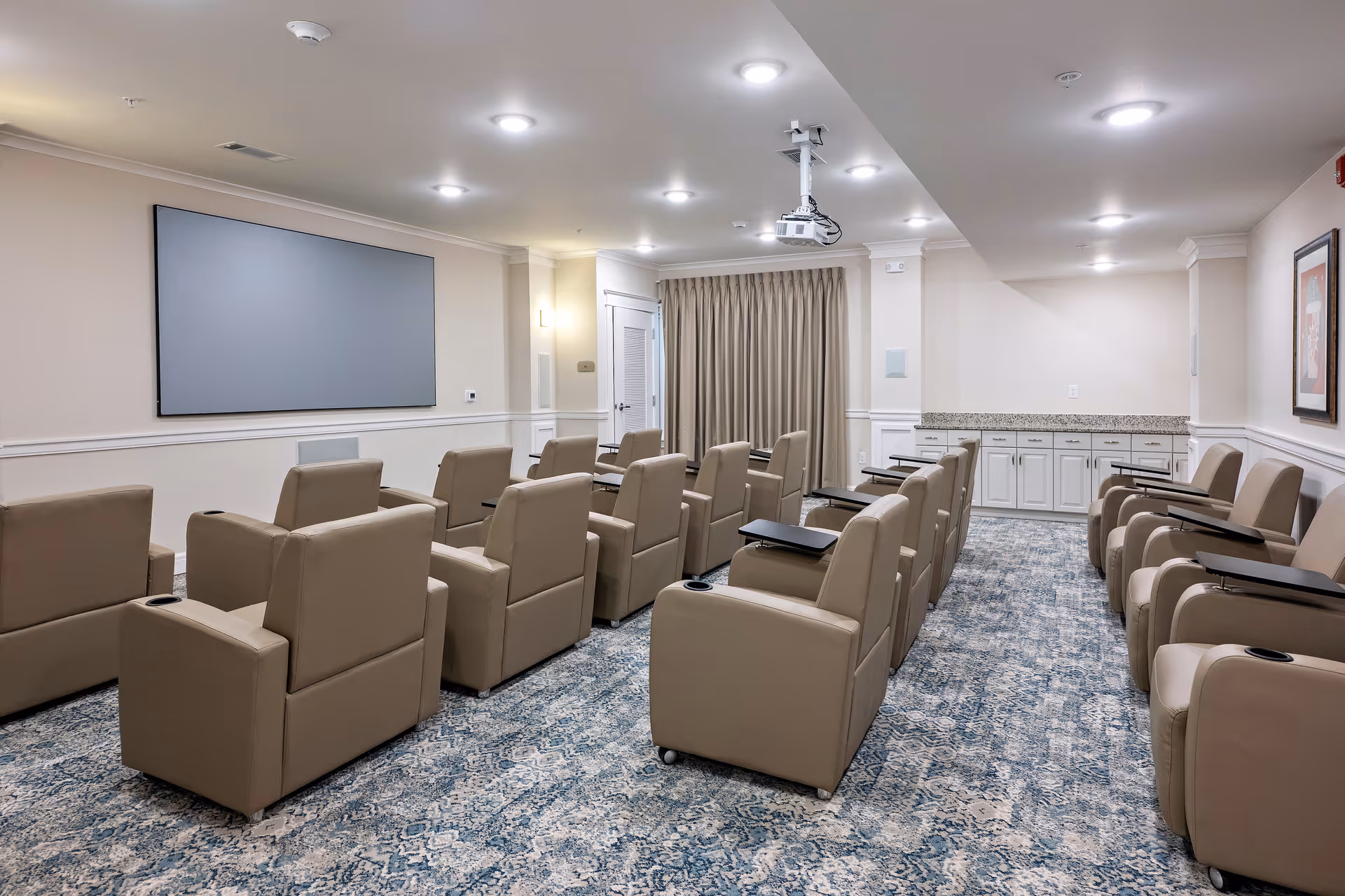 Rows of beige recliner chairs face a large screen in a well-lit conference room.