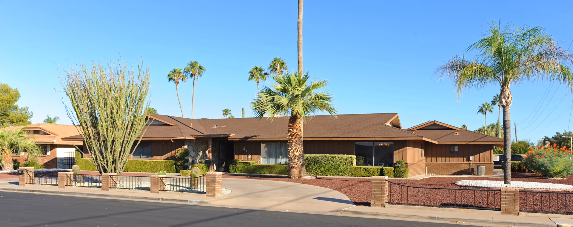Front view of a single-story brown-brick assisted living facility with palm trees.