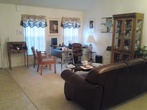 A cozy senior living facility living room with couches, chairs, and a desk.