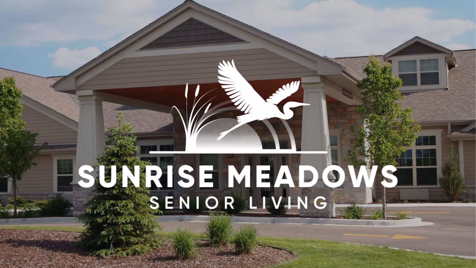 Exterior view of Sunrise Meadows Senior Living entrance with landscaping and logo overlay