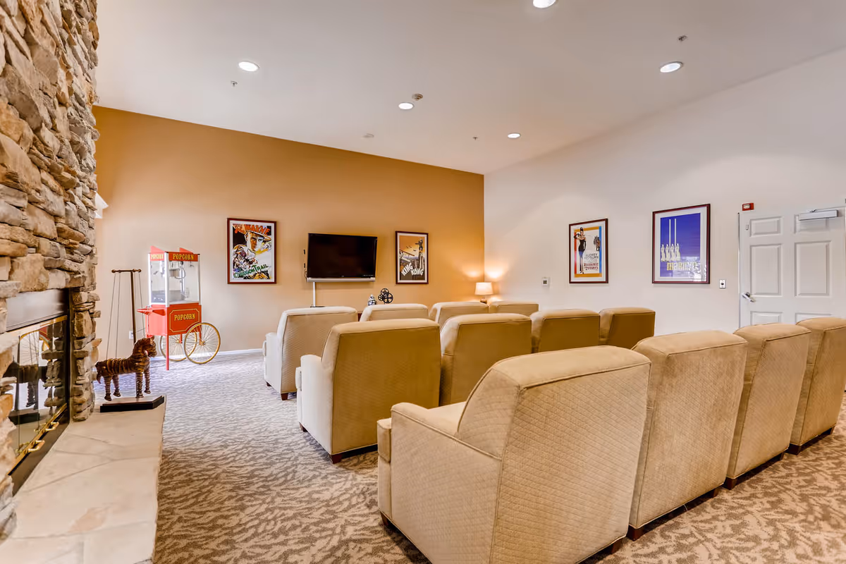 Cozy senior-living lounge with beige seating, a stone fireplace, and wall-mounted TV.