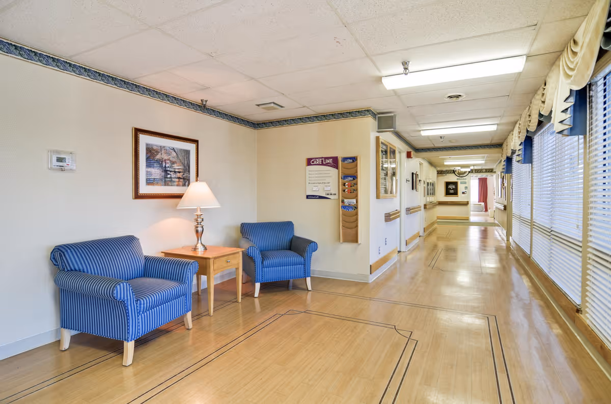 Bright hallway in a senior living facility with blue striped chairs and large windows.