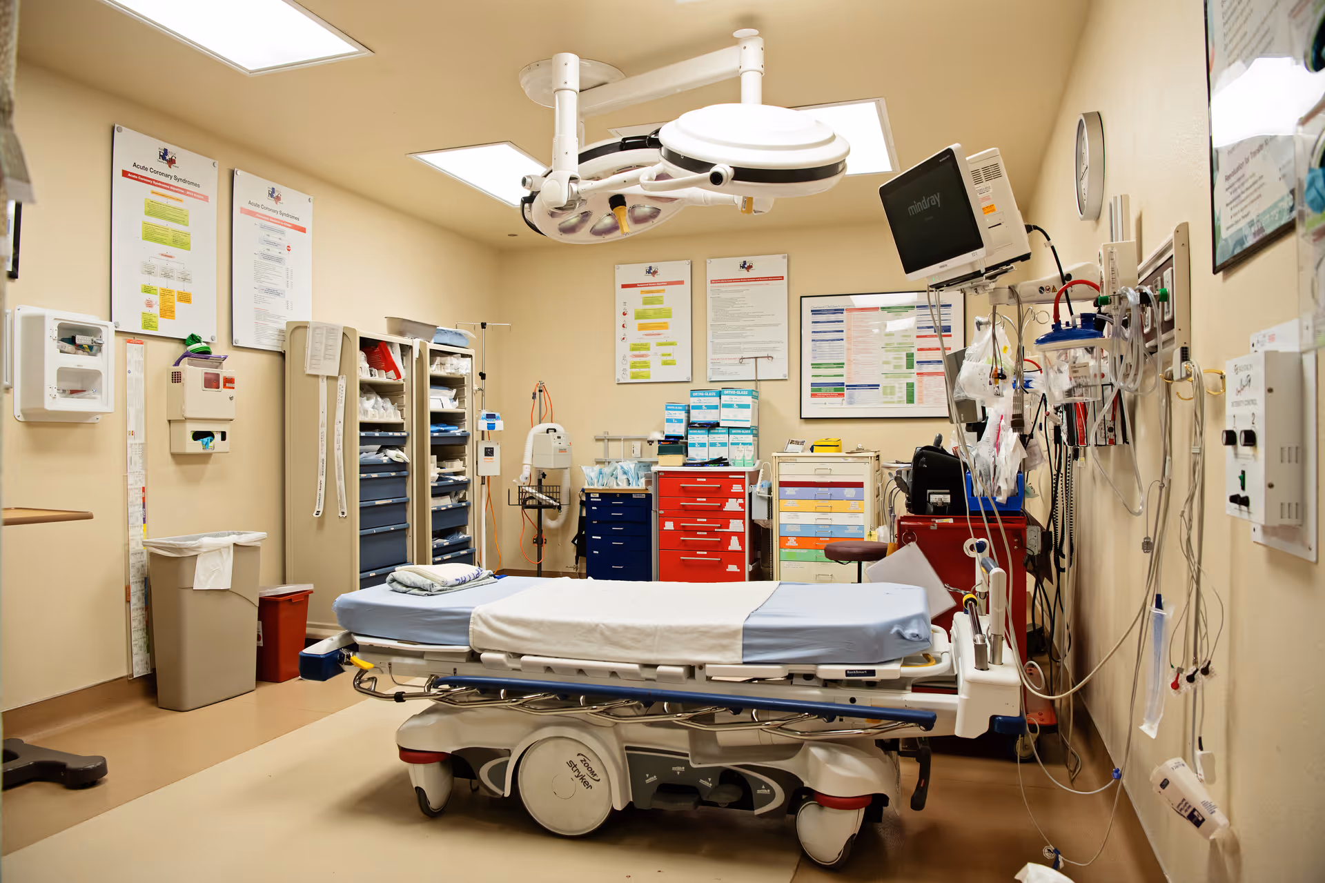 Hospital operating room with a wheeled patient bed, overhead lights, monitors, and medical equipment.