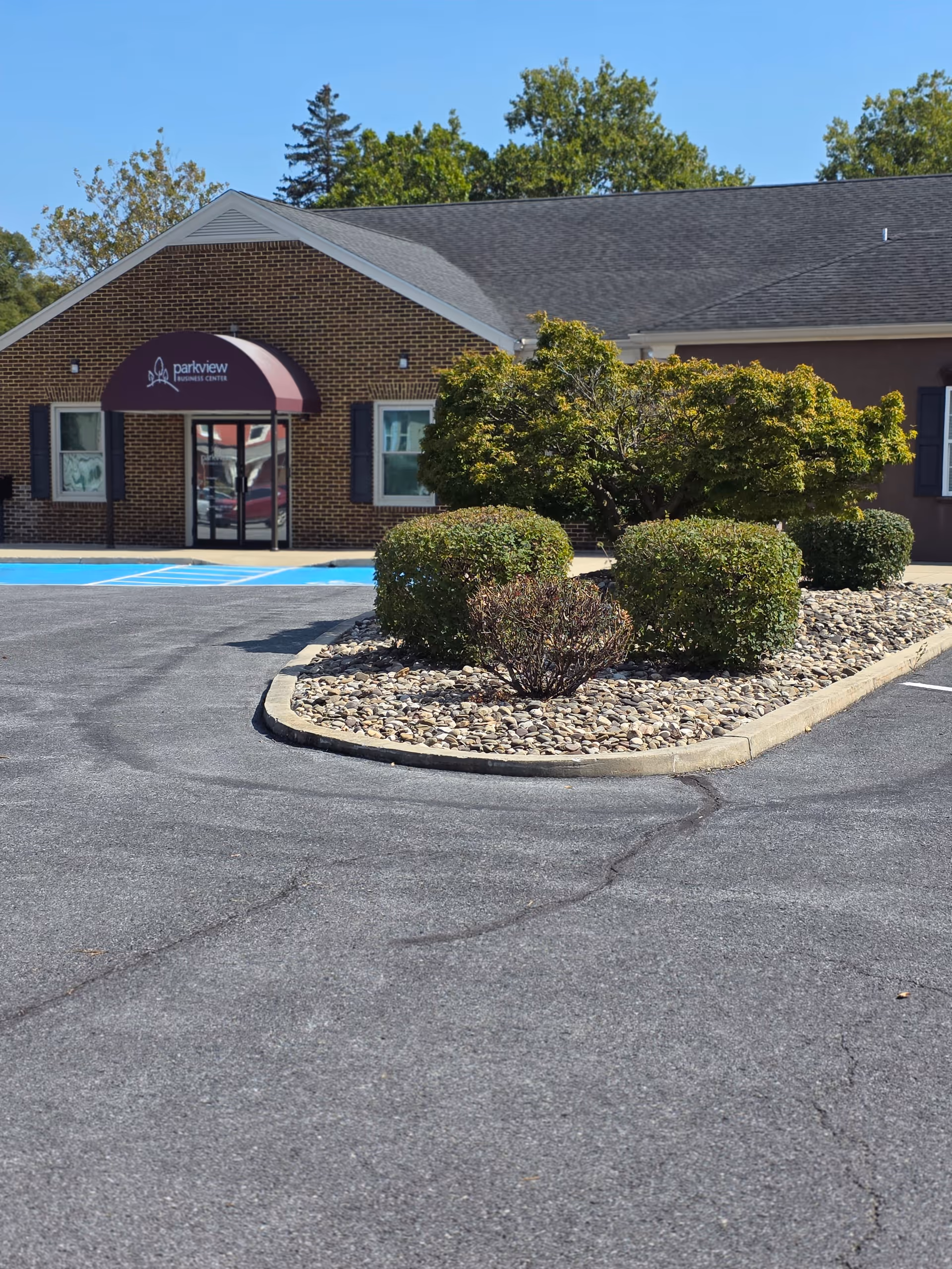 Front view of a brick senior living facility with a purple awning and landscaping.
