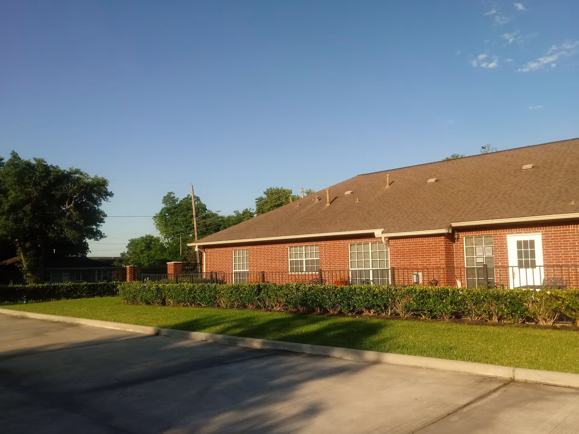 Brick senior living facility with manicured lawn and hedges under a blue sky.