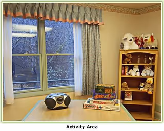 Activity area with a table, radio, puzzles, and stuffed animals by a window.