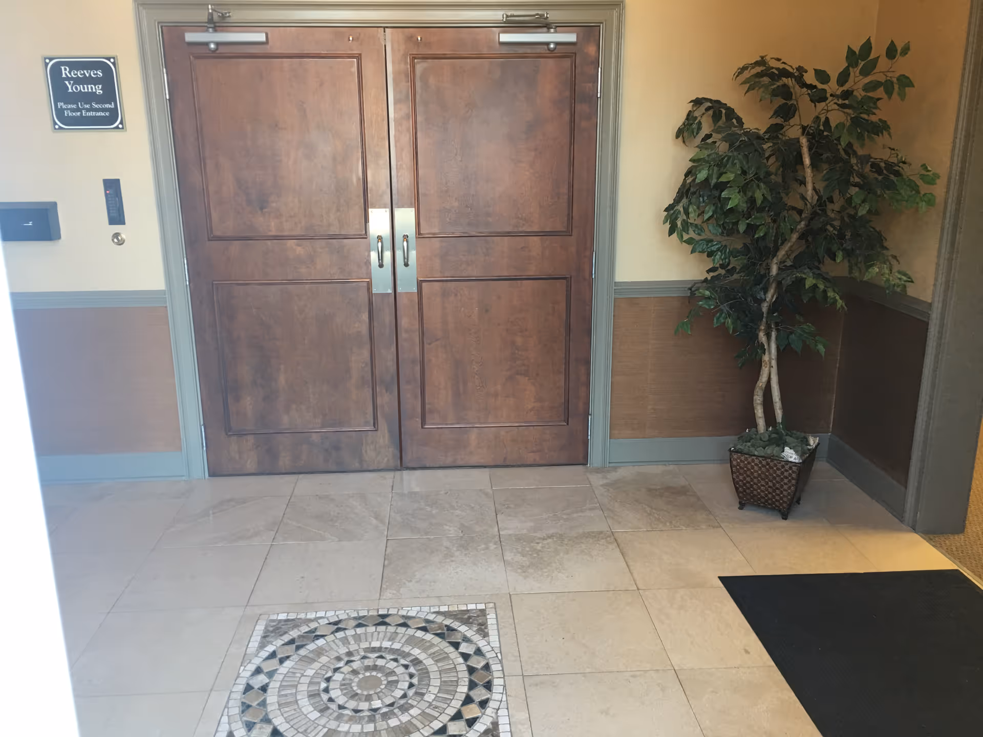 Double wooden doors in a hallway with a potted plant and tiled floor.