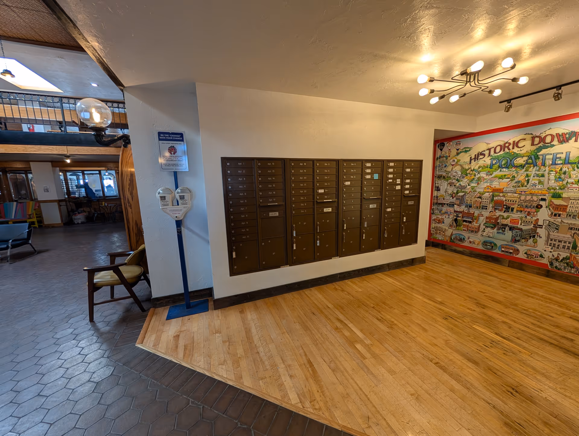 Interior lobby area with a row of metal mailboxes, wooden floor, and colorful mural.