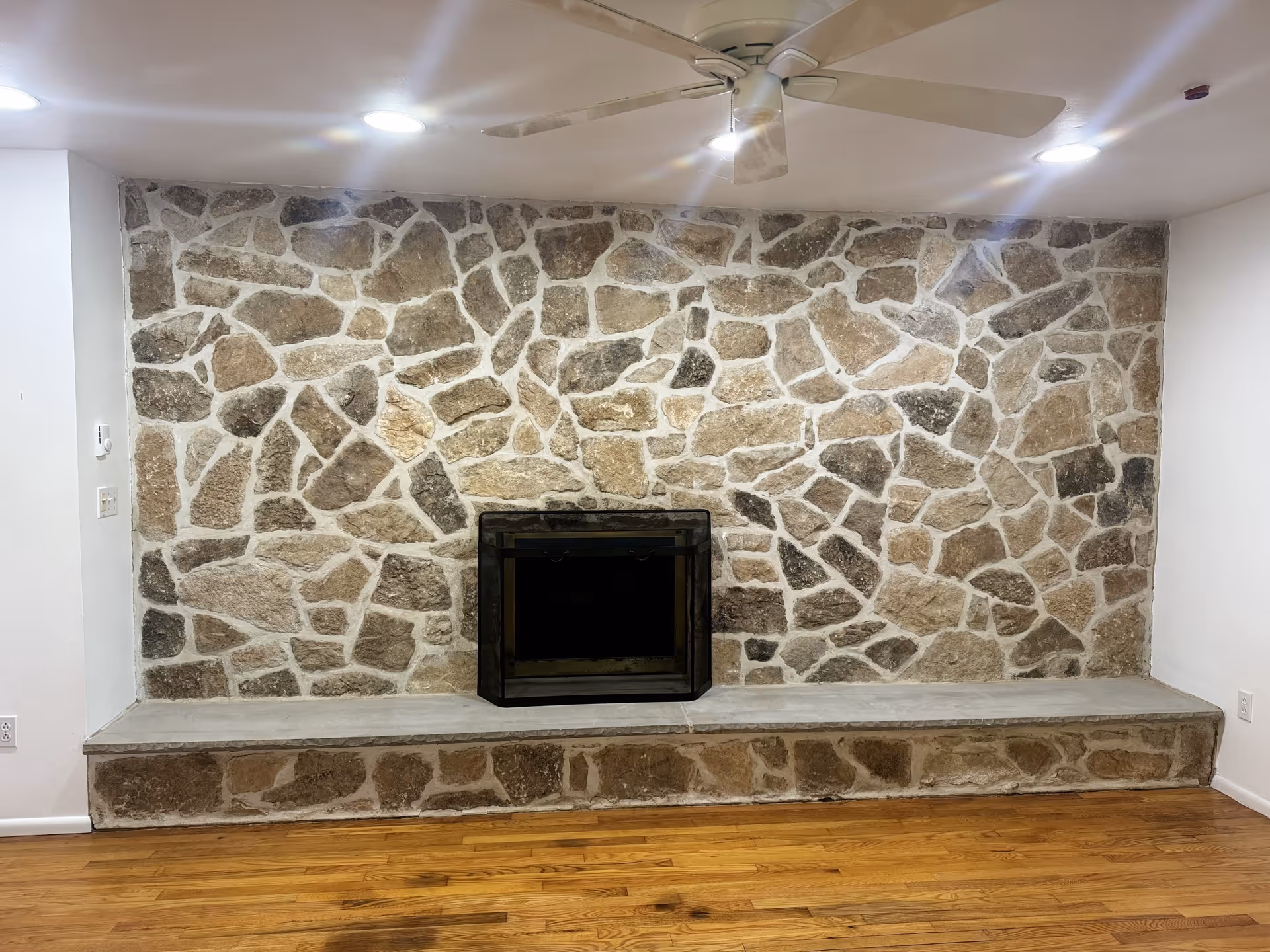 Stone fireplace centered on a stone wall with a raised concrete hearth.
