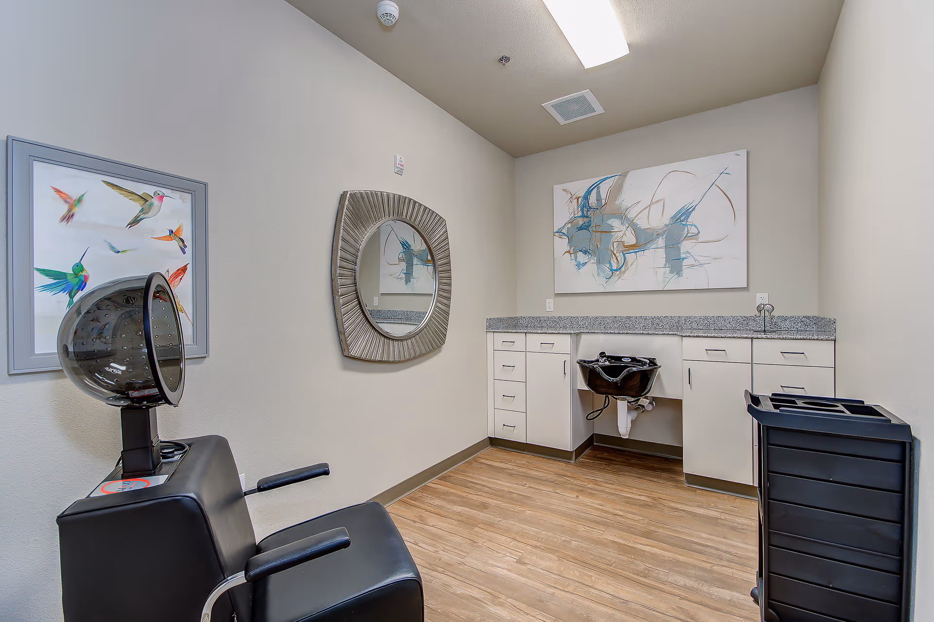 Hair salon area inside a senior living facility with a hood dryer, mirror, and counter.