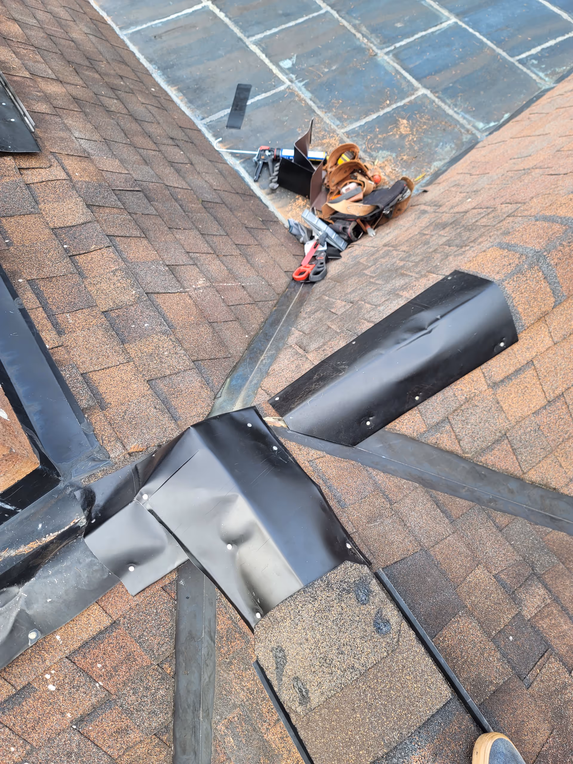 A rooftop with brown shingles, metal flashing, and scattered tools.