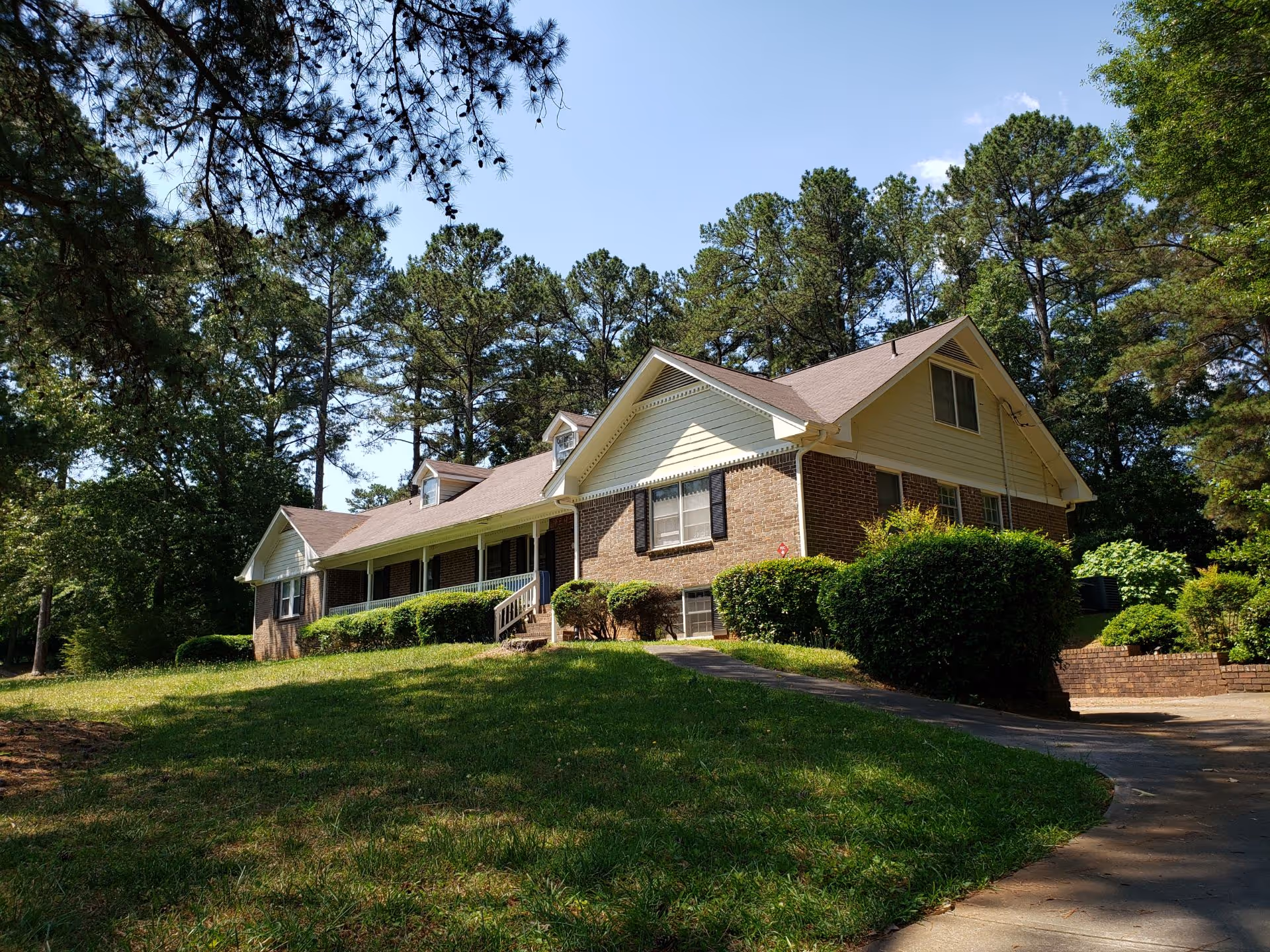 Brick senior living facility with a pitched roof, front porch, and surrounding mature trees.