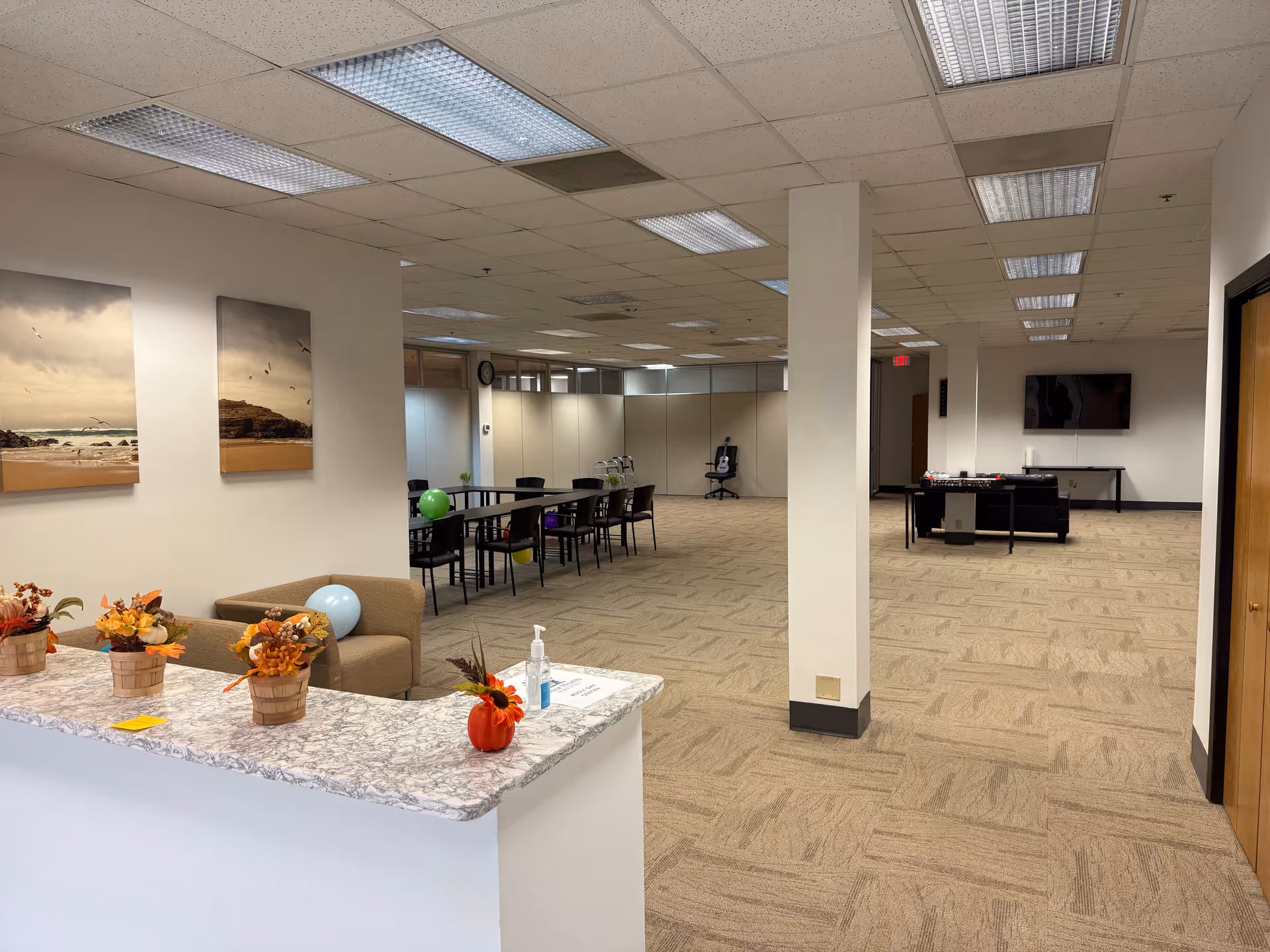 A spacious, well lit lobby featuring a marble reception counter, seating, balloons, and a game area.
