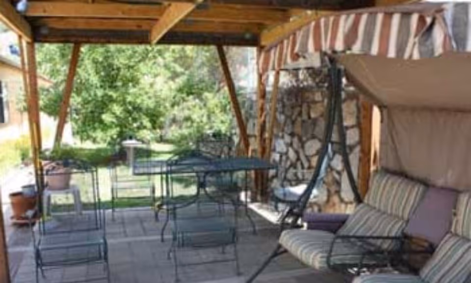 Covered outdoor patio with striped awning, metal chairs, a swing, and garden in background