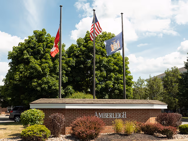 Exterior view of The Amberleigh entrance sign with flags and landscaping.