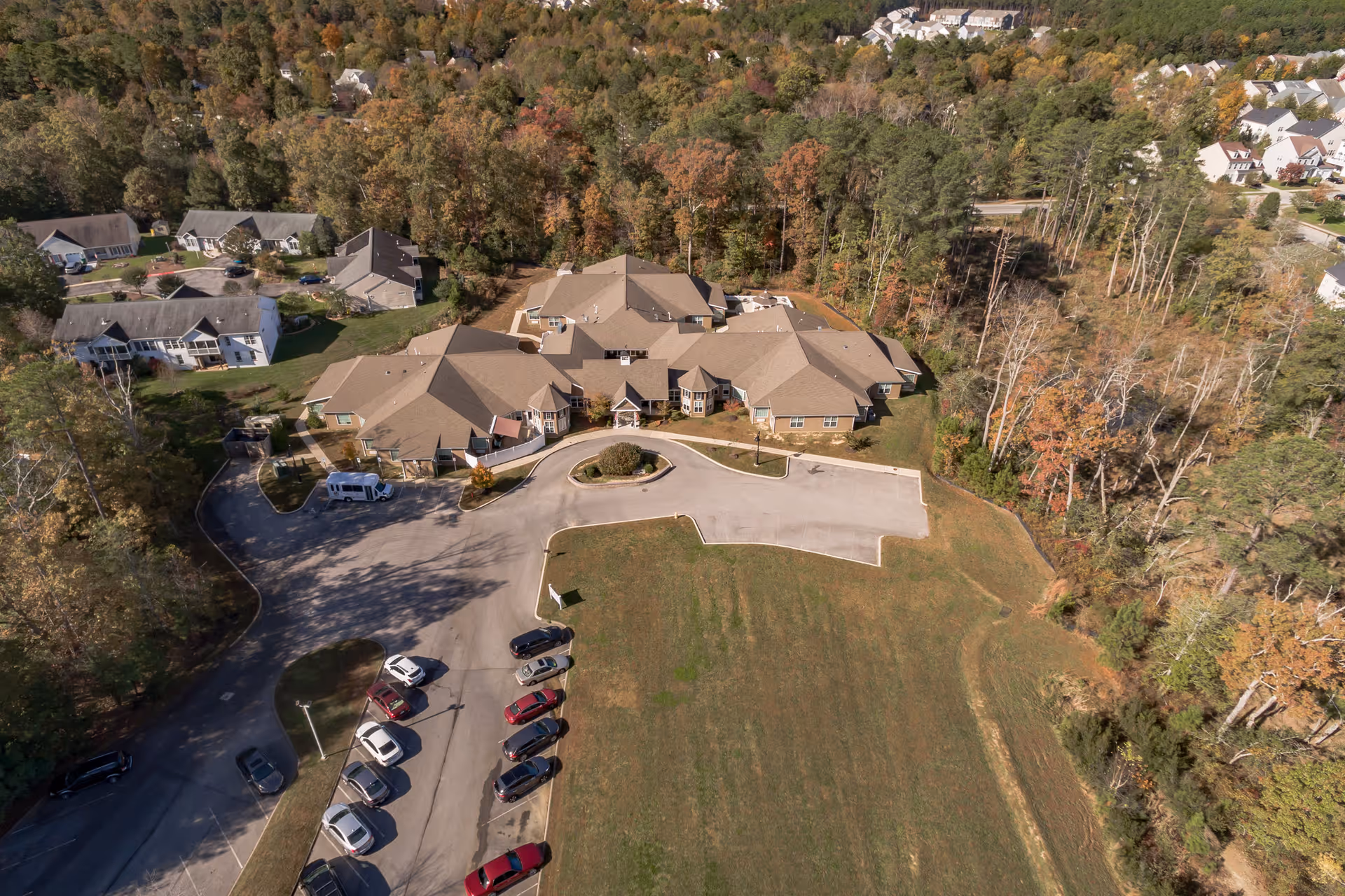 Aerial view of Discovery Commons At Wildewood facility surrounded by trees and residential houses, with a parking lot in front and a large grassy area adjacent to the building.
