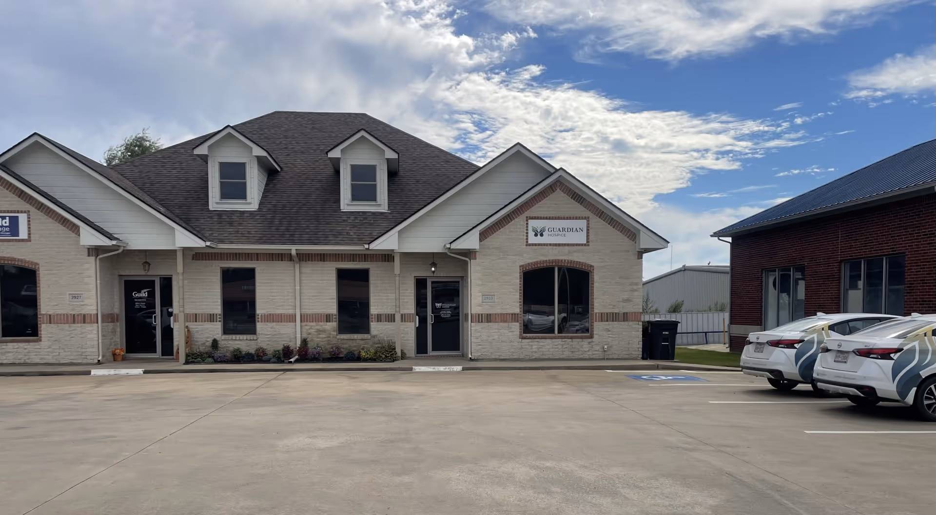 Front exterior view of Guardian Hospice building with brick facade and parked cars.