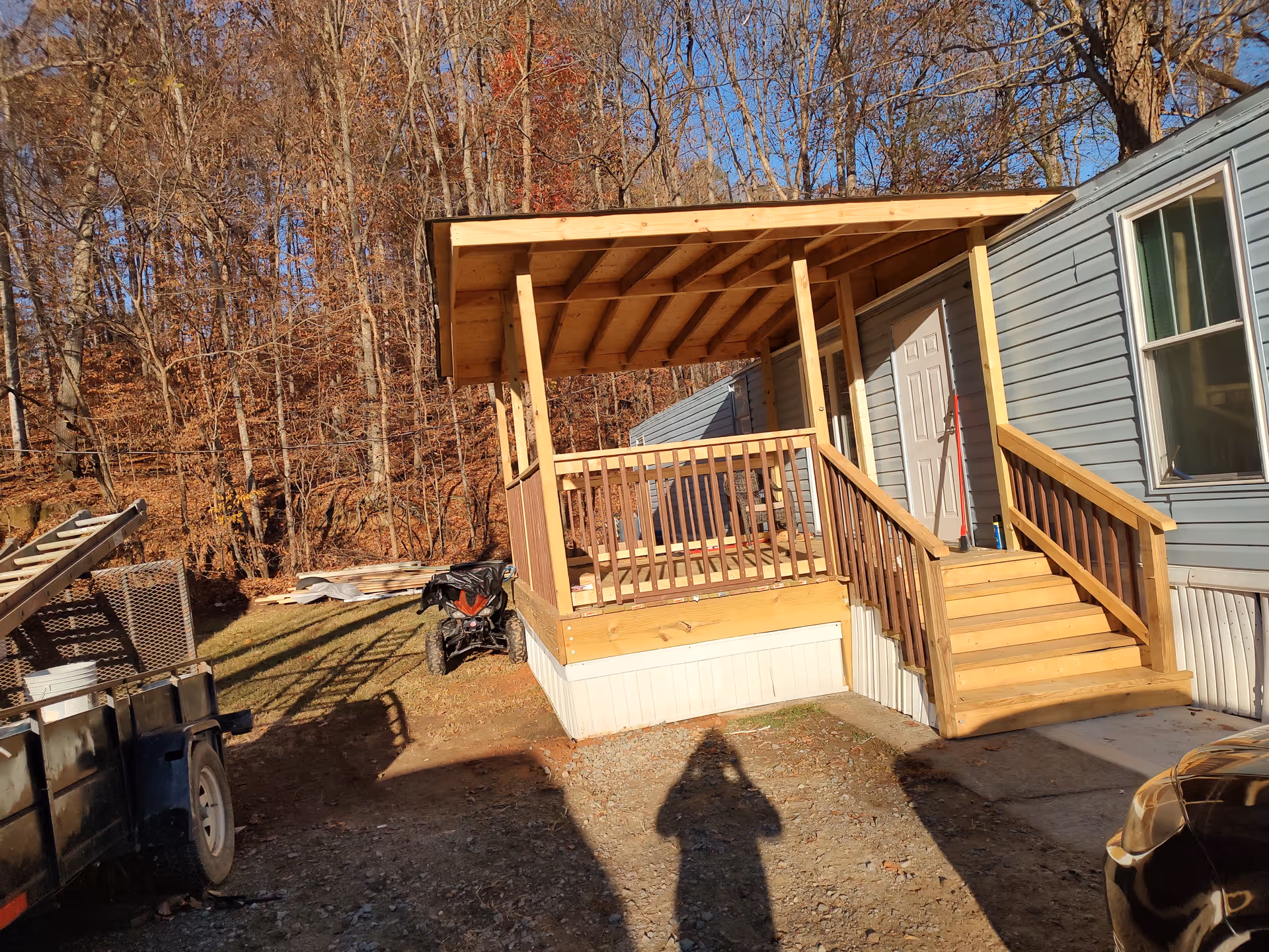 Wooden covered porch deck attached to a blue mobile home, with stairs and railing.