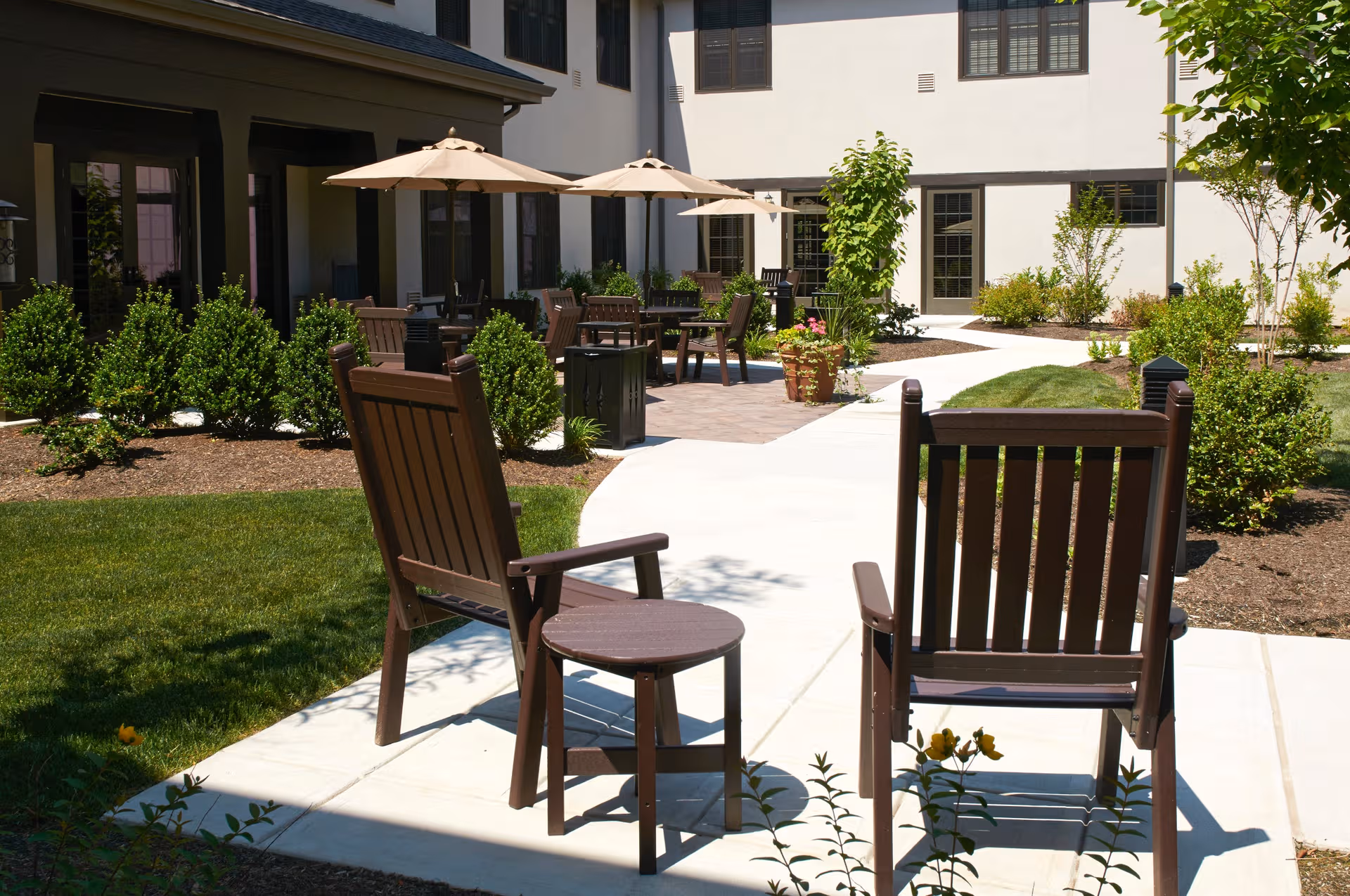 Outdoor courtyard of a senior living facility with wooden chairs, tables, and umbrellas.
