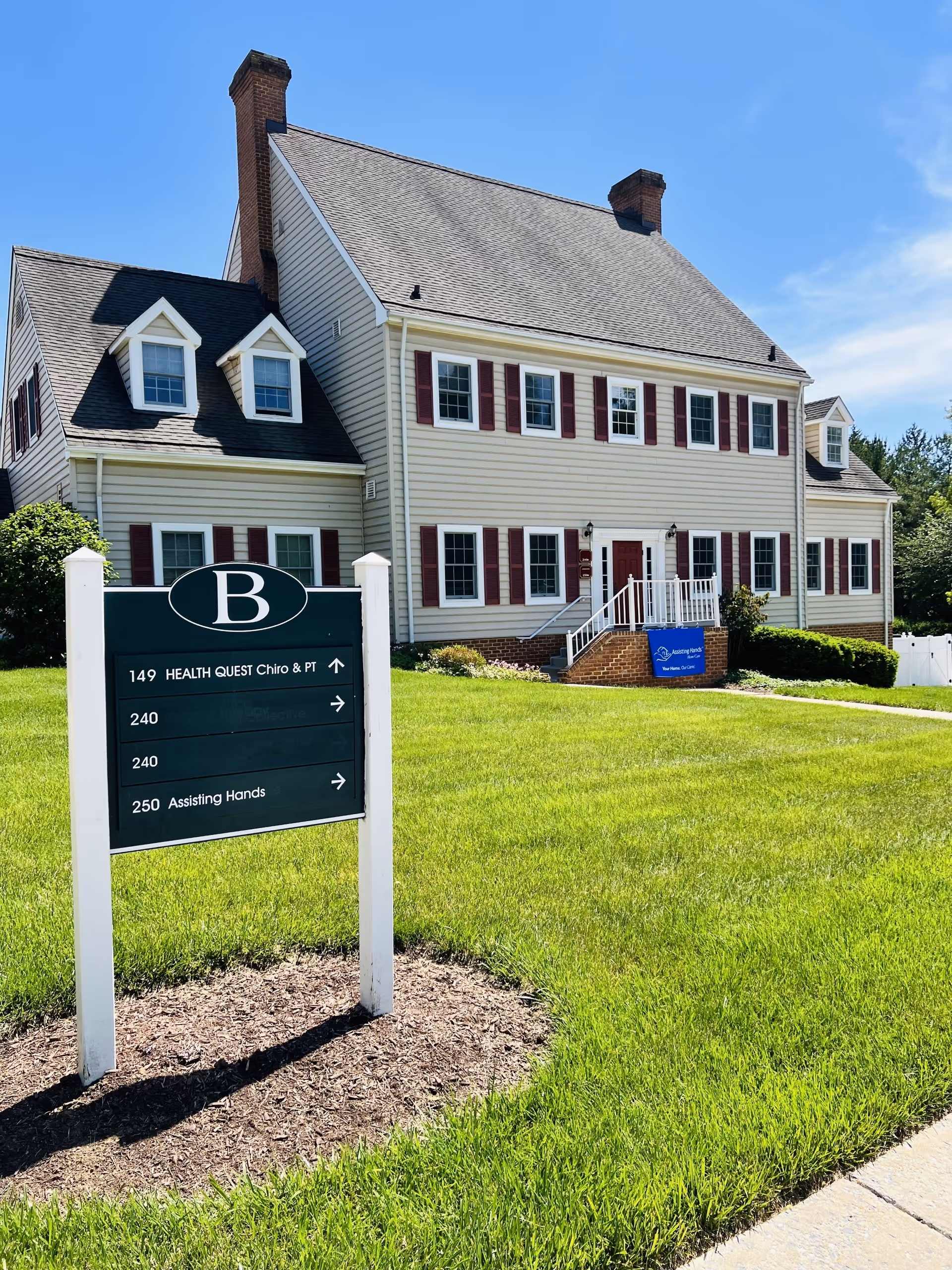 Exterior view of Assisting Hands facility: a two-story beige house with red shutters and front sign.