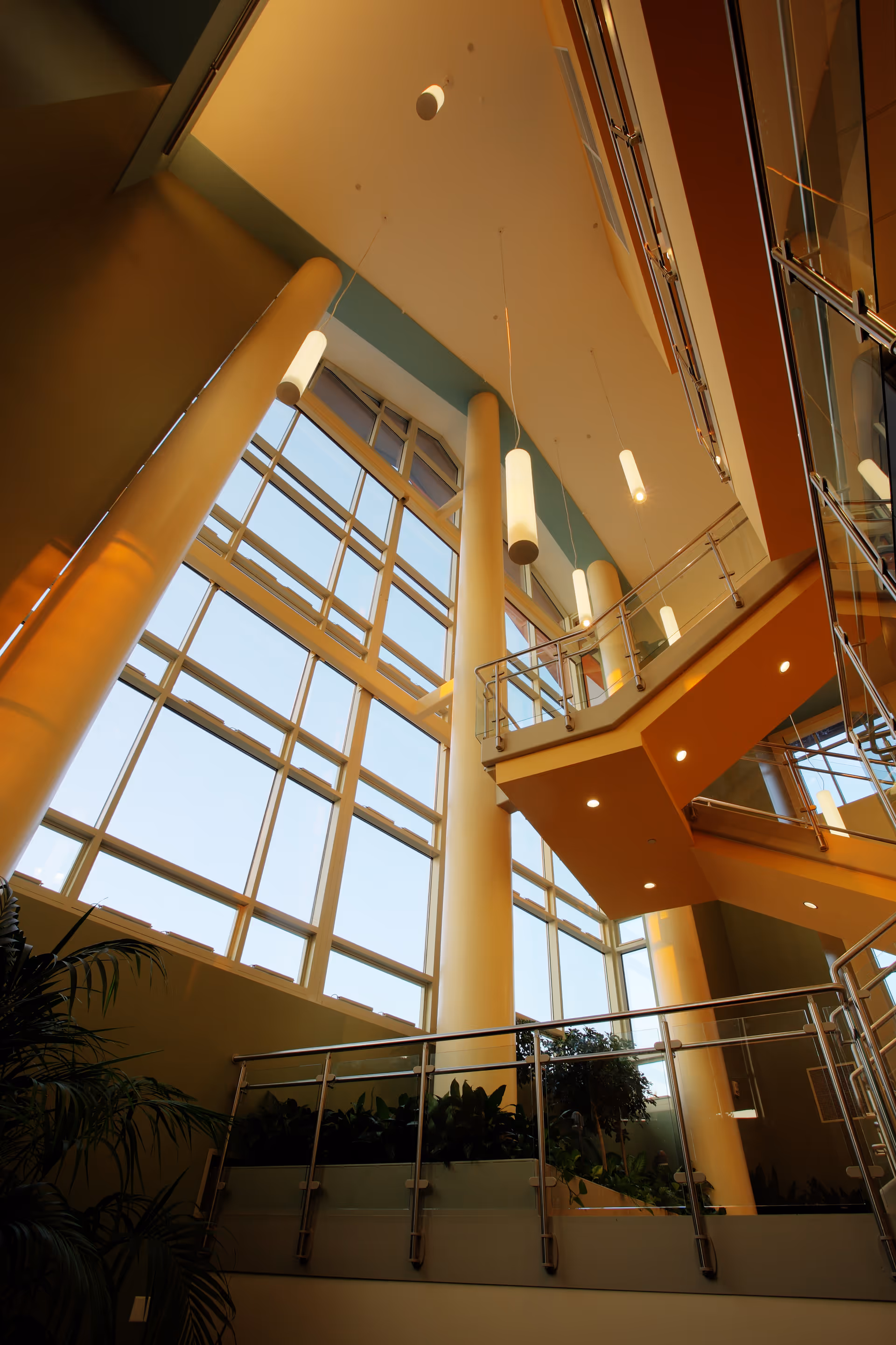 Tall atrium interior with large glass windows, yellow columns, and a suspended staircase.