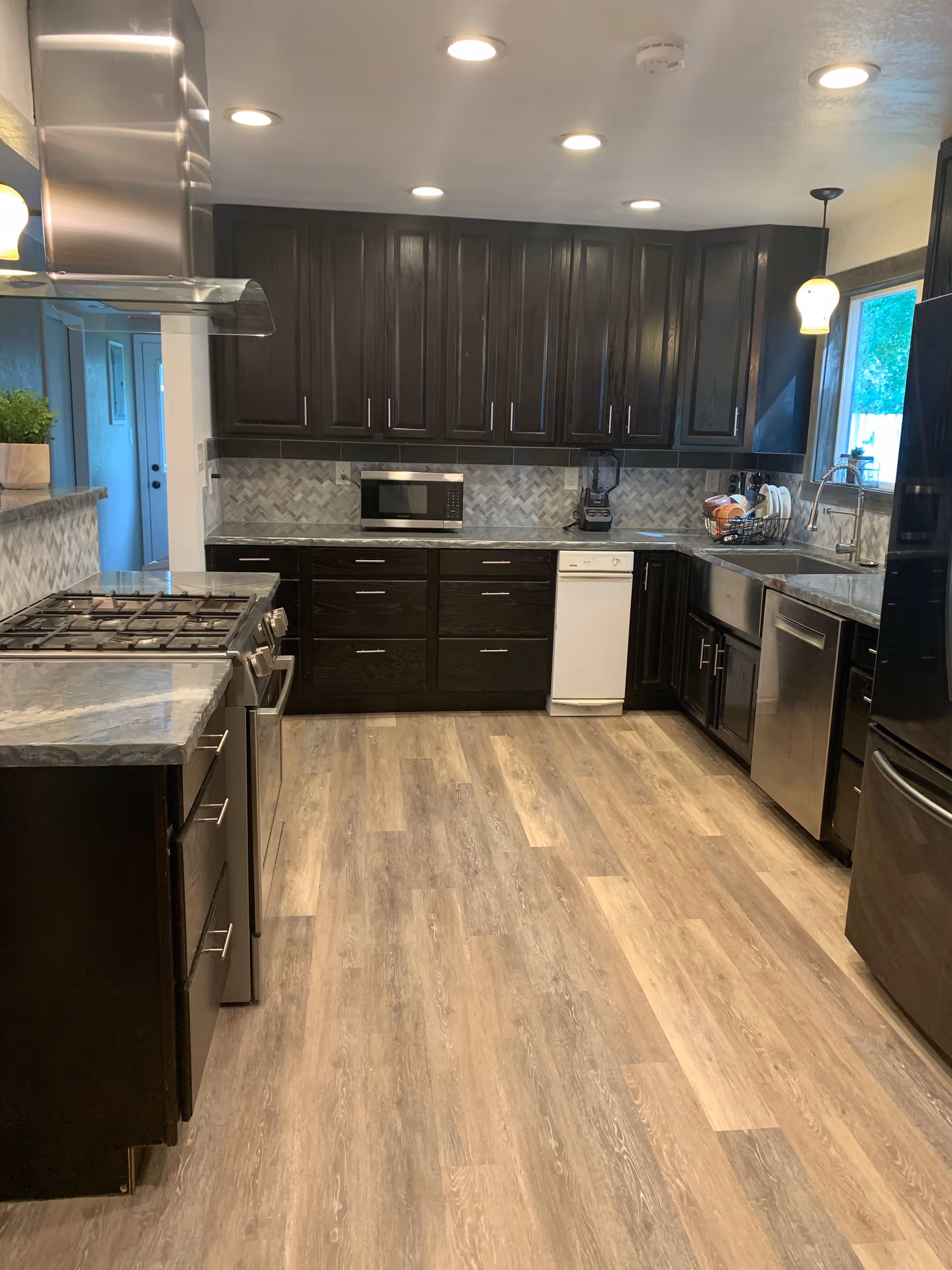 A modern galley kitchen with dark cabinets and stainless steel appliances.