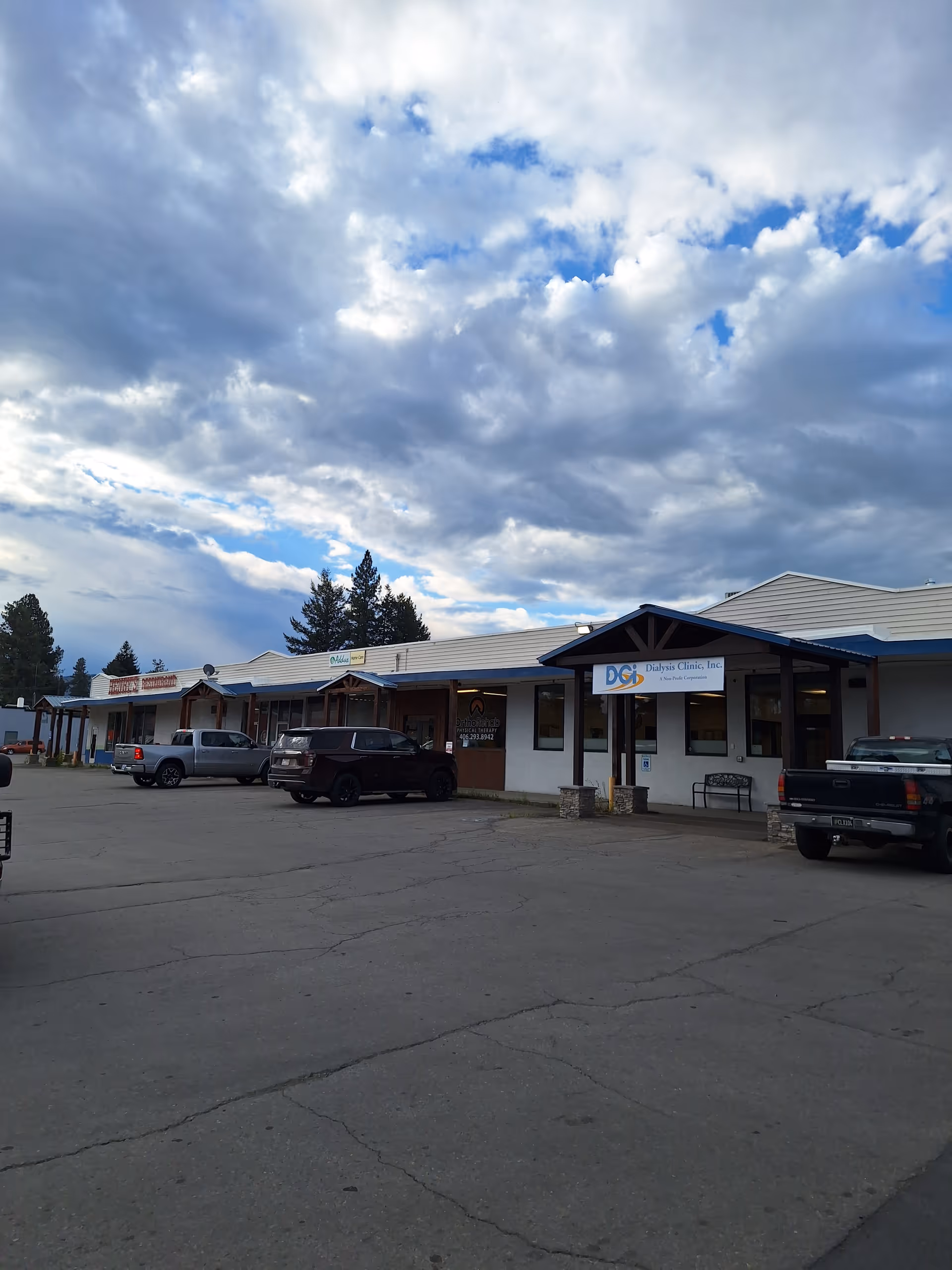Exterior of a single-story strip-style building with parked cars and cloudy sky.