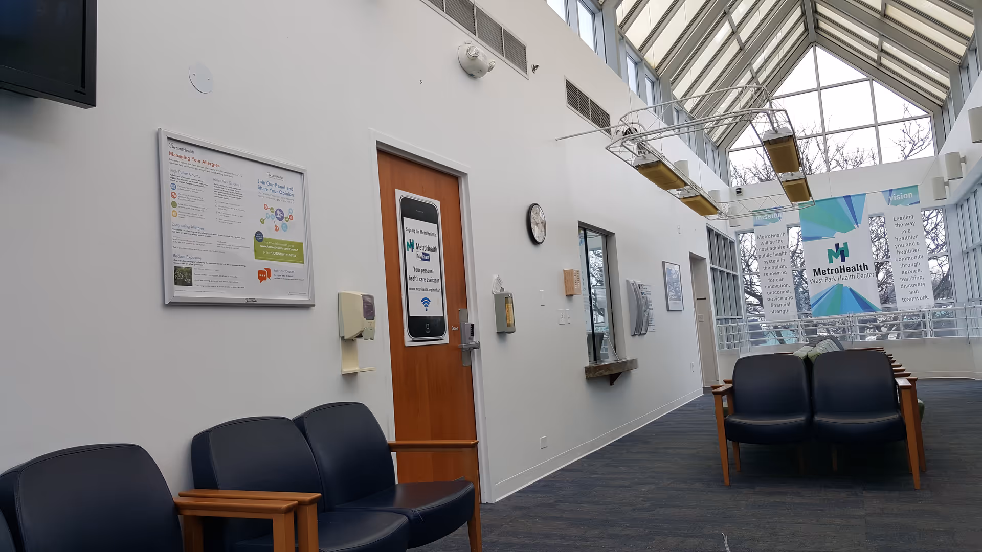 Interior hallway of MetroHealth West Park Health Center with couches, glass skylight ceiling, banners.