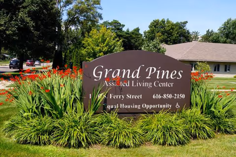 Sign reading Grand Pines Assisted Living Center surrounded by flowers outdoors.
