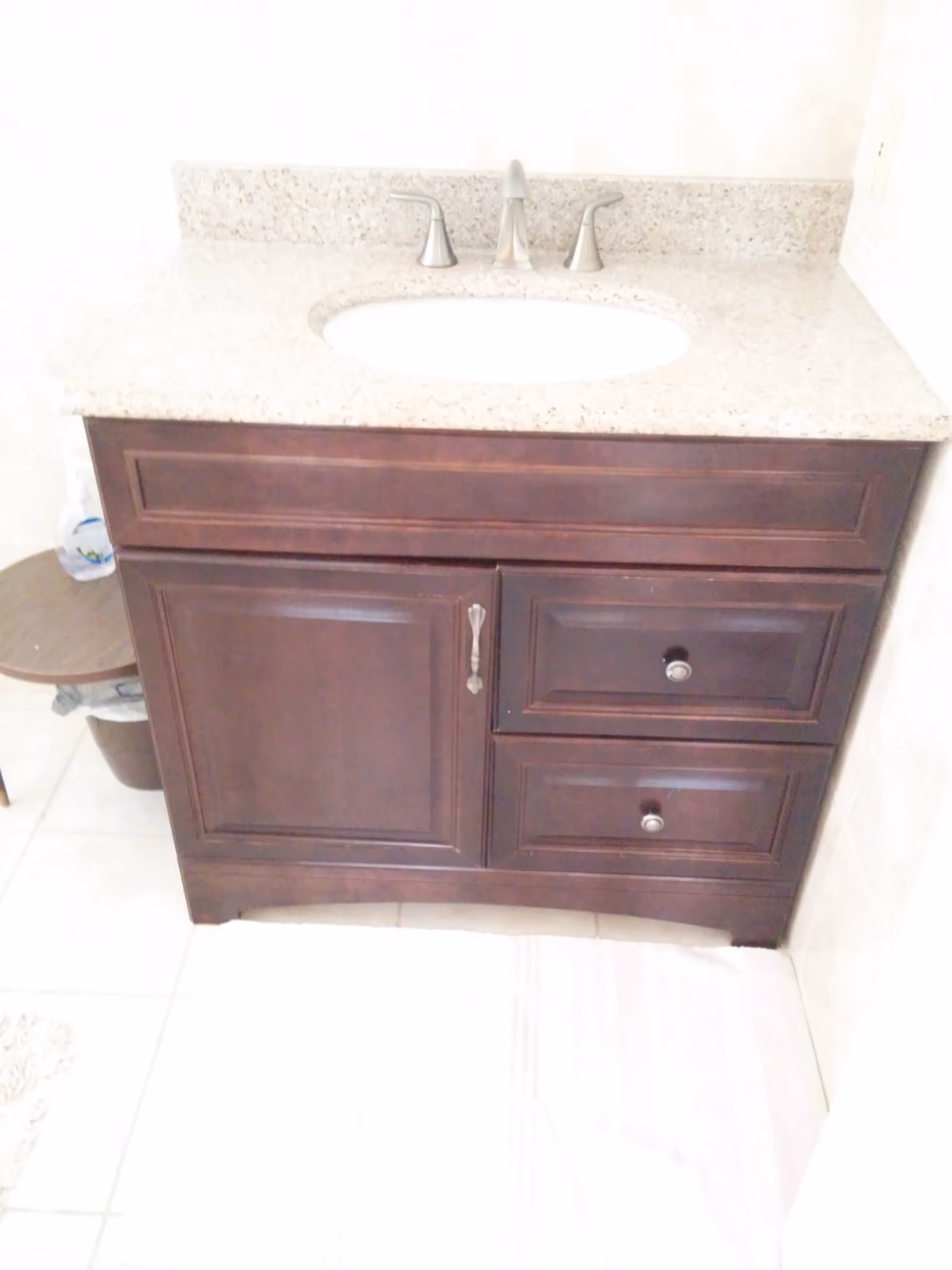 A bathroom vanity with a granite countertop, oval sink, chrome faucet, and a dark wood cabinet with drawers.