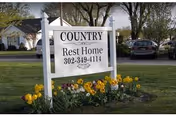 A Country Rest Home sign sits in front of a building with yellow flowers.