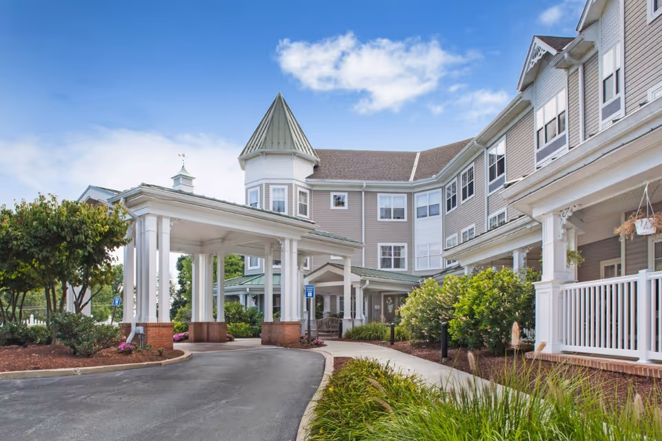 Front entrance and porte-cochère of a multi-story senior living building with landscaping and a driveway.