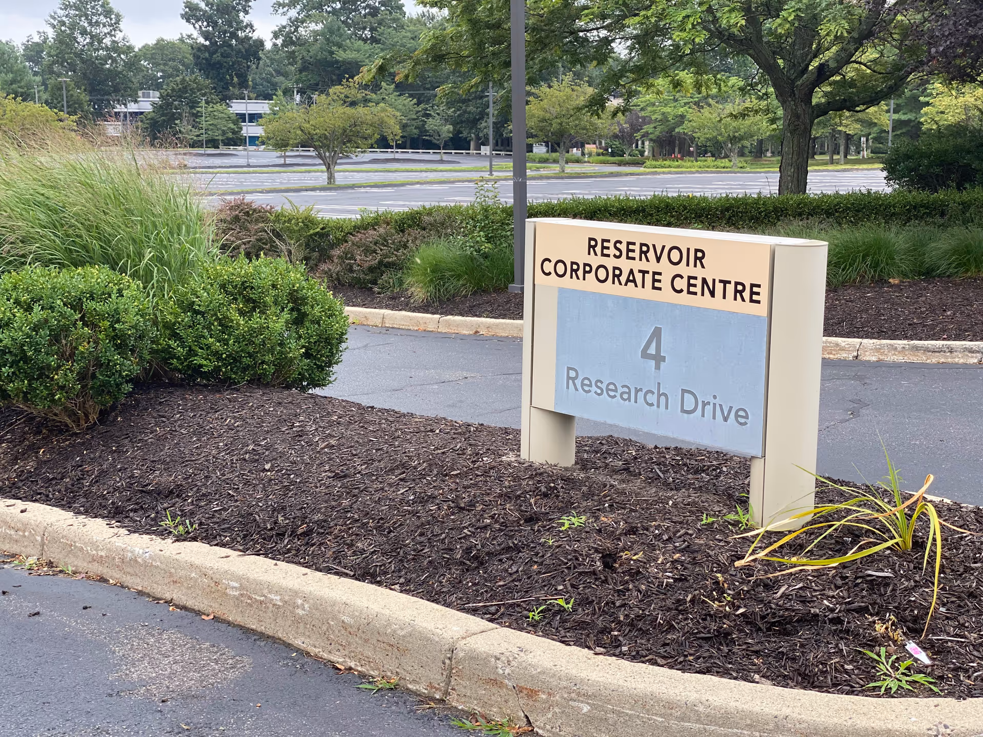A landscaped parking lot with a beige sign for Reservoir Corporate Centre on Research Drive.