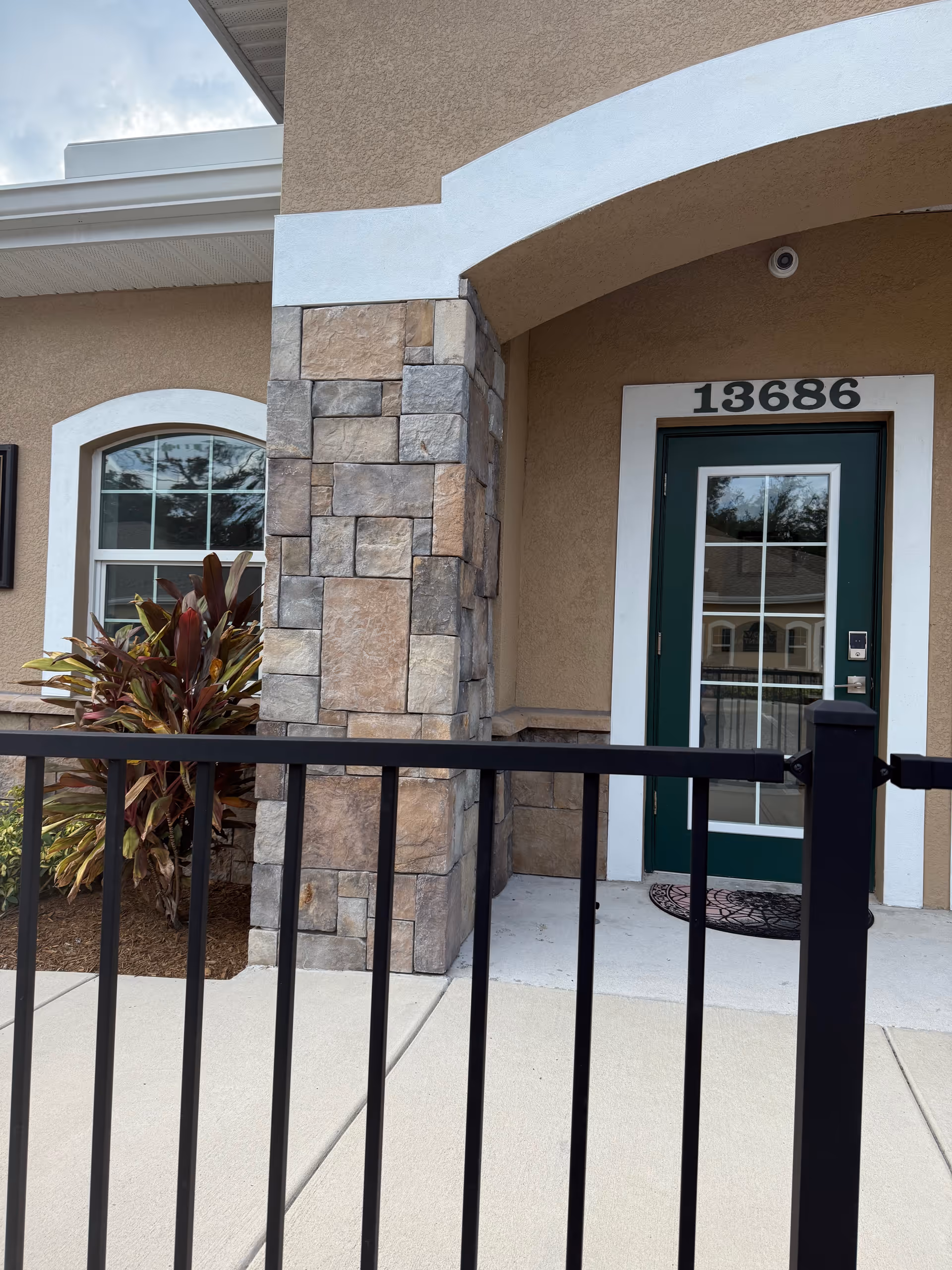 Front entrance of a senior living facility with beige walls, stone pillar, green door, address 13686