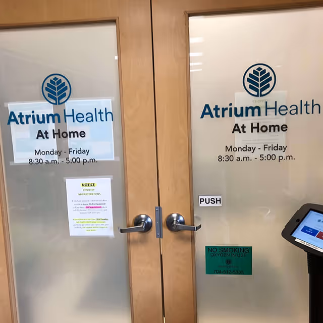 Double glass doors with Atrium Health At Home signage and hours posted.