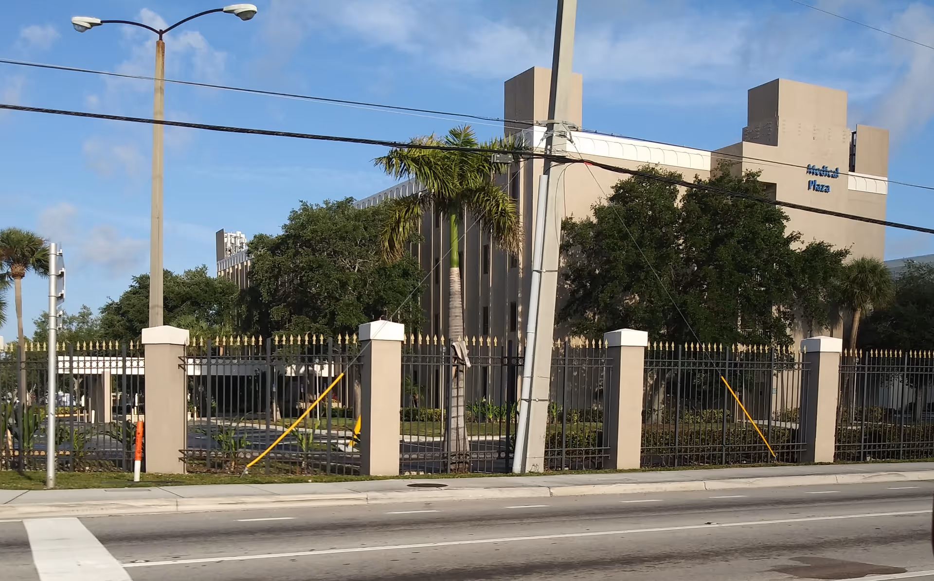 Exterior view of a gated facility with palm trees and a modern building facade.