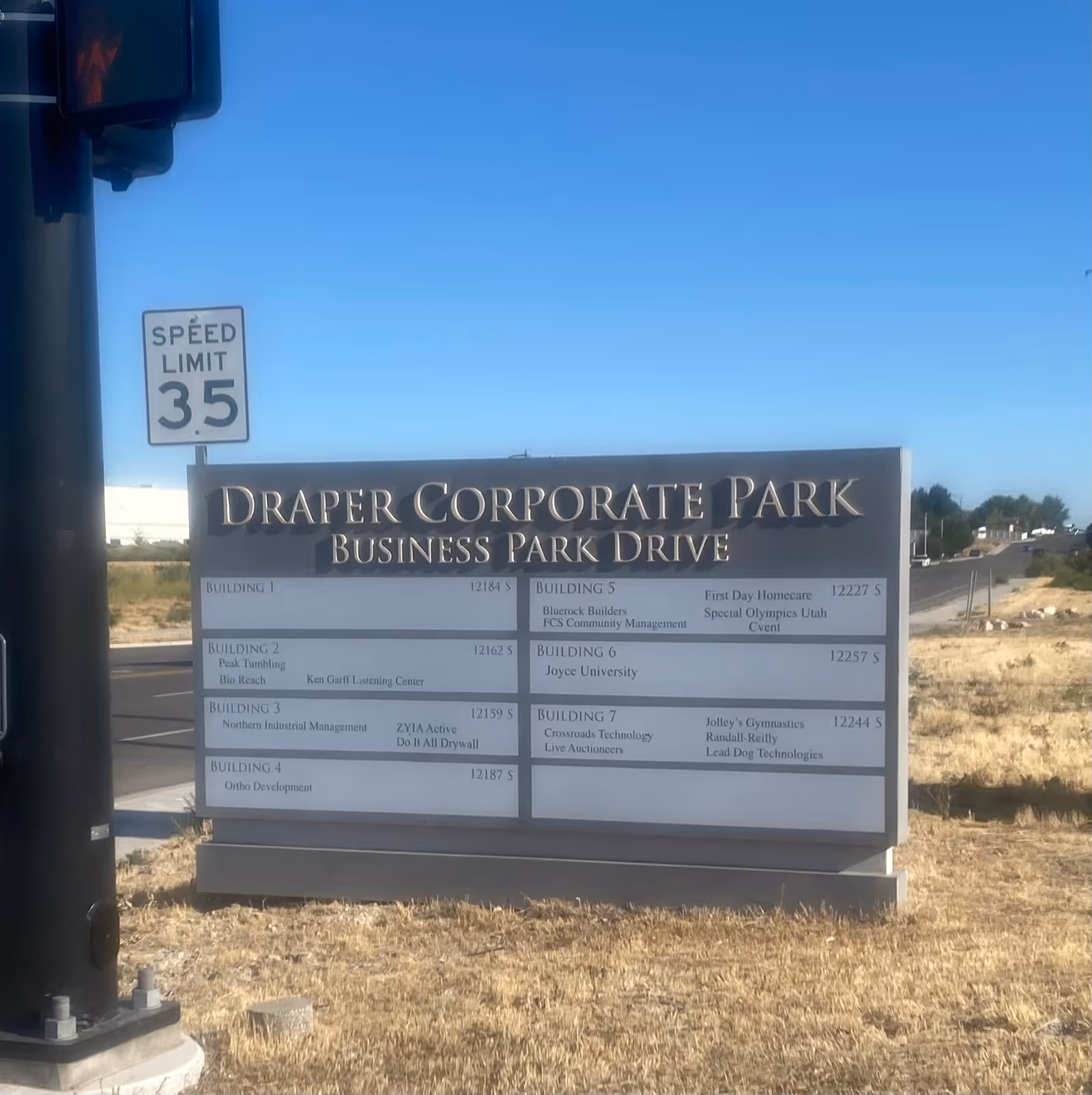 Outdoor street scene with a Draper Corporate Park sign and listings, under a clear blue sky.