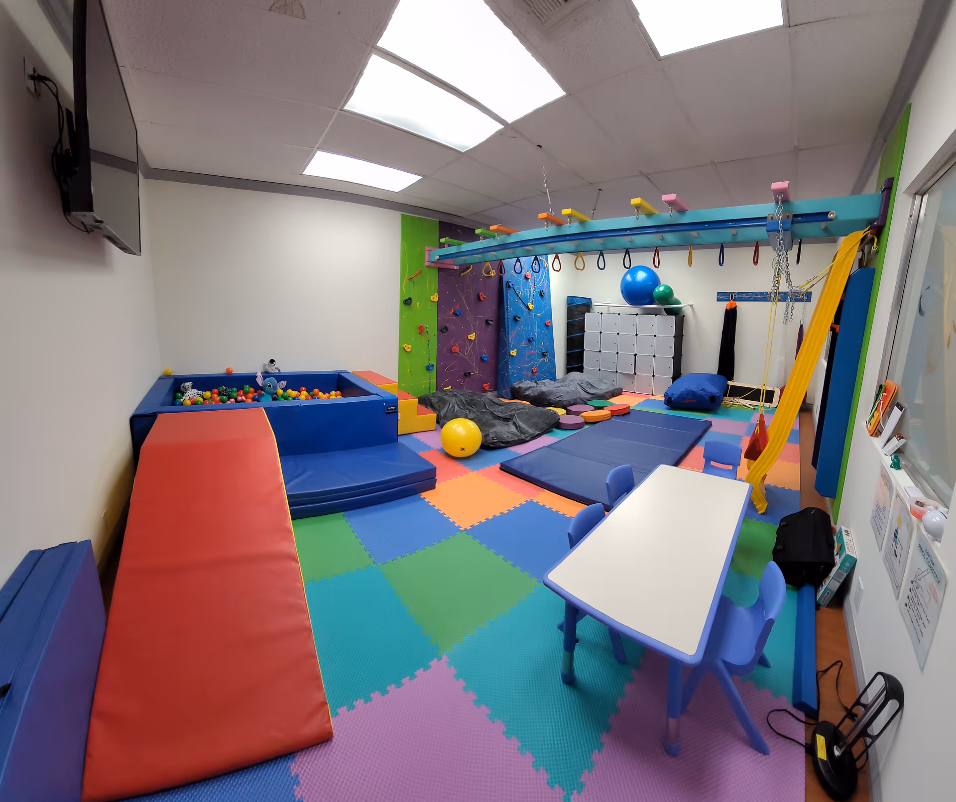 Colorful indoor activity room with foam mats, a ball pit, climbing wall, and play equipment.