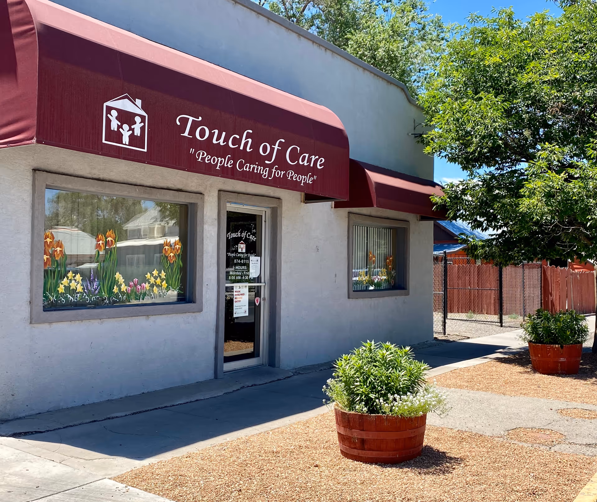 Exterior view of Touch of Care facility with maroon awnings, windows, and potted plants.