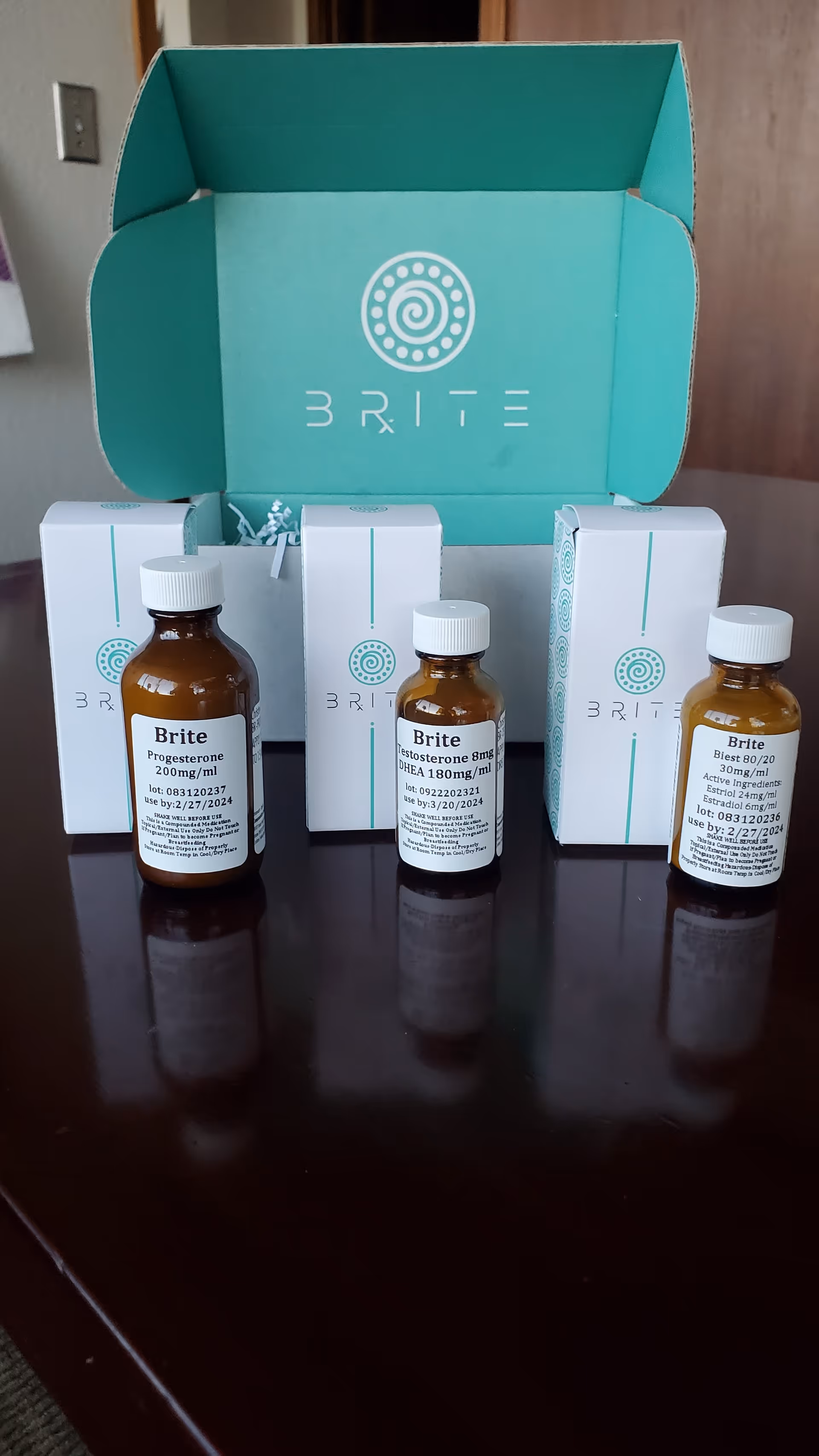 Open teal BRITE box with three bottle vials labeled Brite on a dark wooden table.