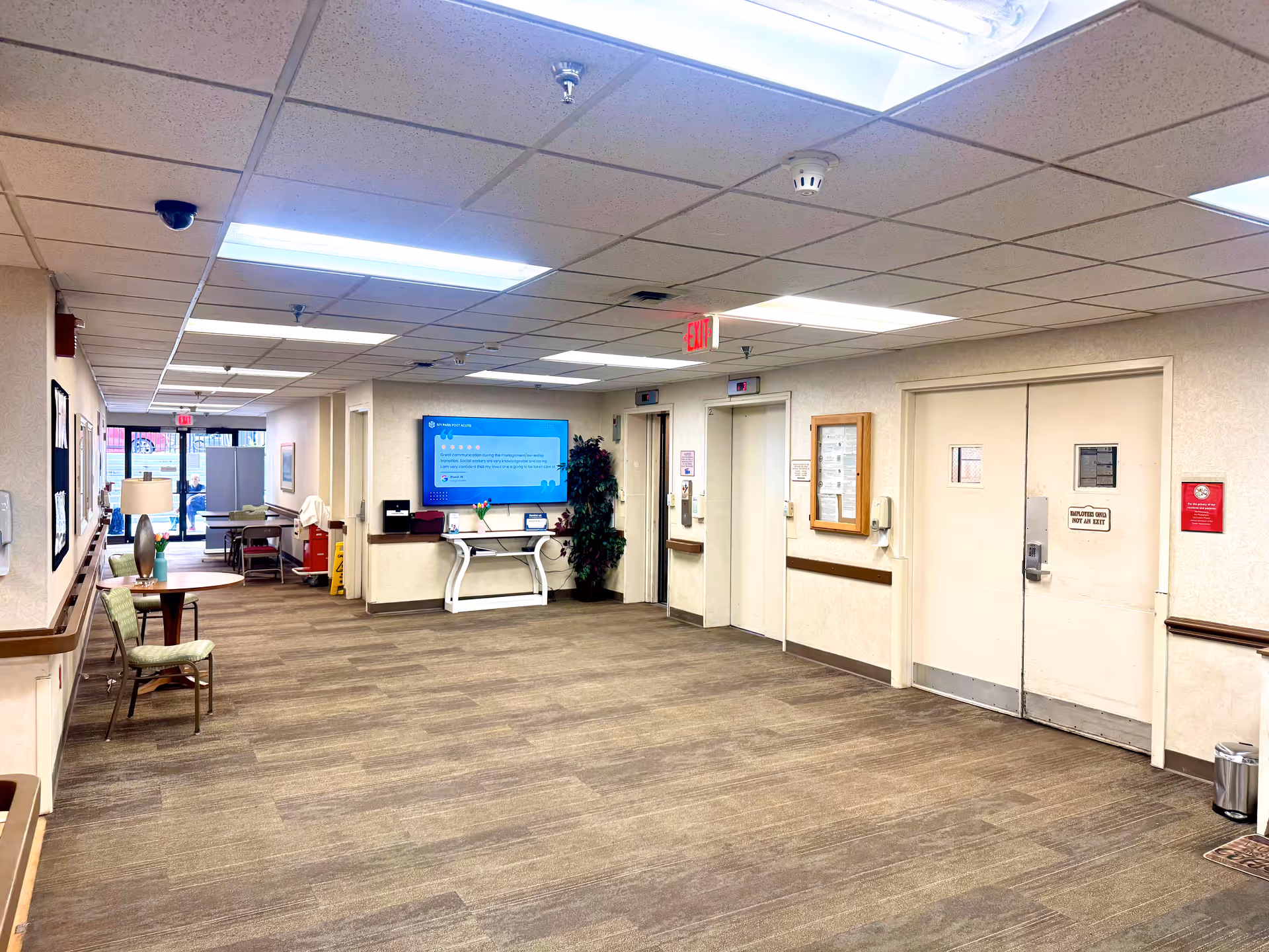 A long hallway in a senior living facility with seating, a TV, and doors.