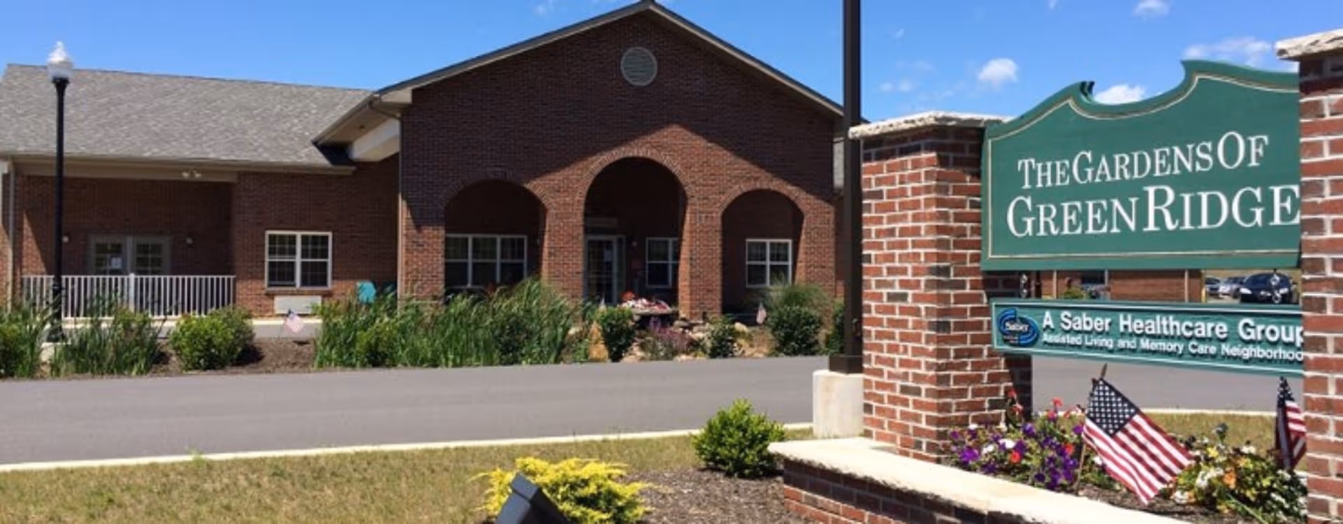 Front view of The Gardens of Green Ridge exterior with brick arches, sign, and landscaping.